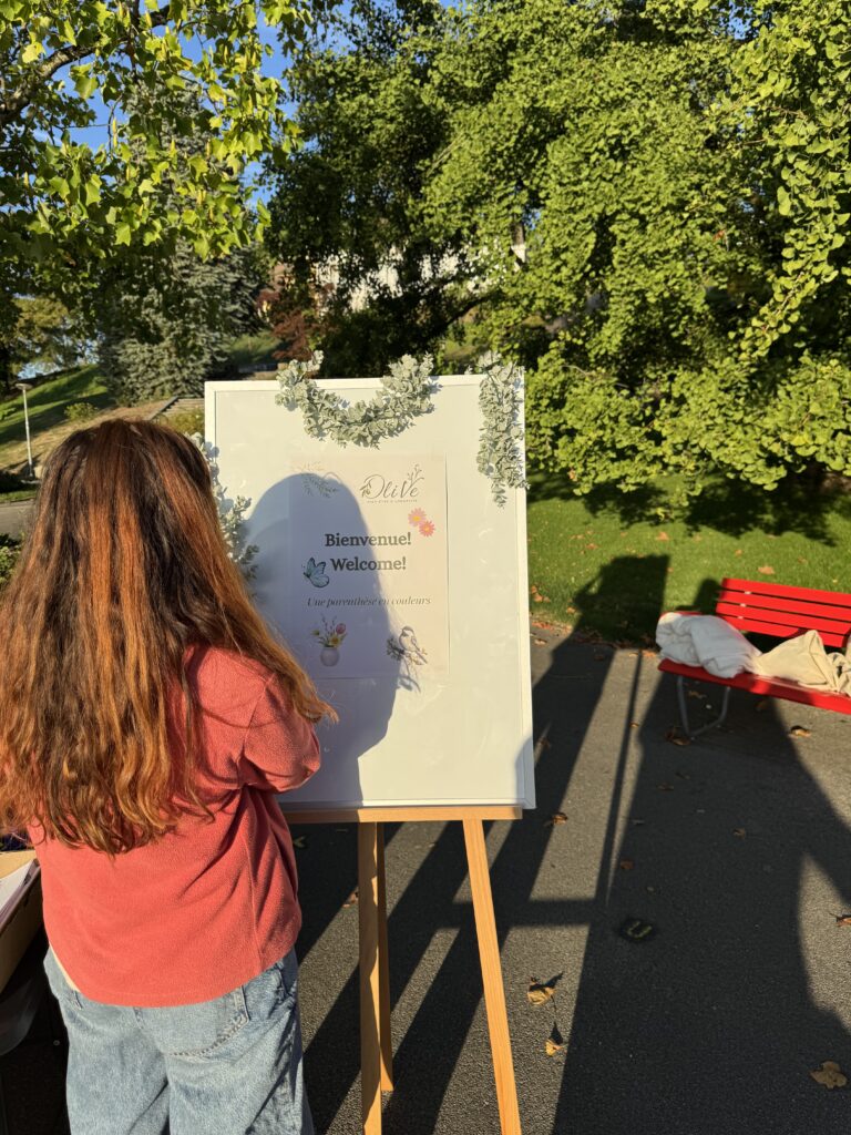 Une participante devant le panneau de bienvenue de l’atelier, posé sur un chevalet dans un parc.