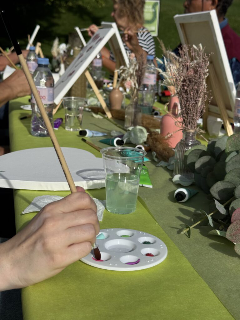Une main trempe un pinceau dans une palette, au milieu des chevalets et des bouquets.