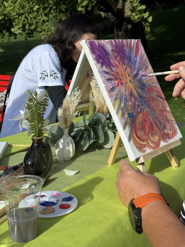 Une participante peint une fleur aux couleurs vives sur une toile posée sur un petit chevalet.