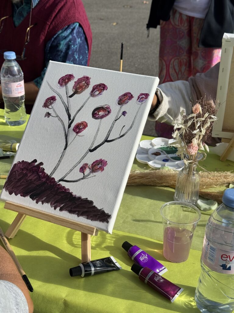Toile en cours : une branche de fleurs pourpres, entourée de tubes de peinture.