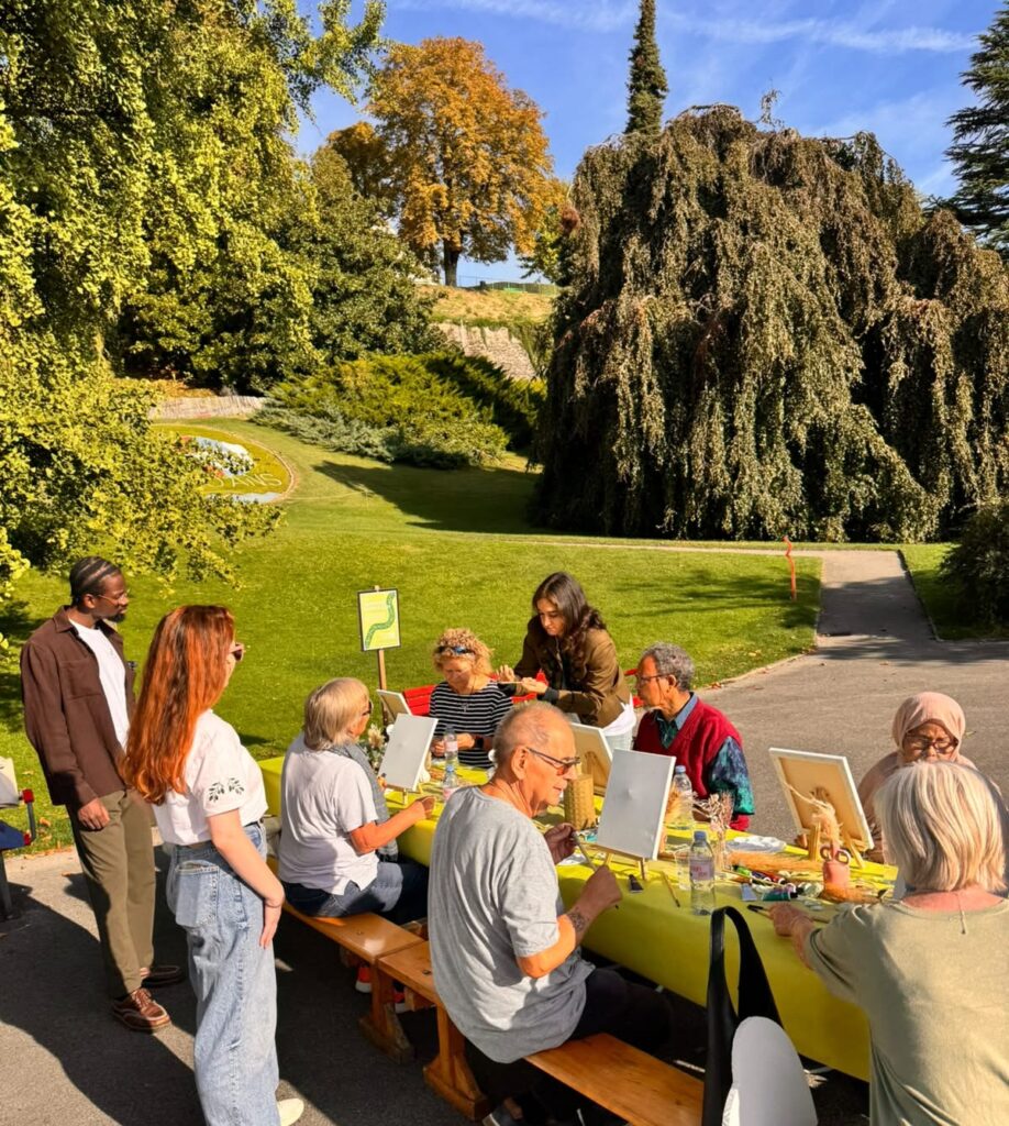 Atelier de peinture en plein air : des participants réunis autour d’une longue table, dans un parc de Nyon.